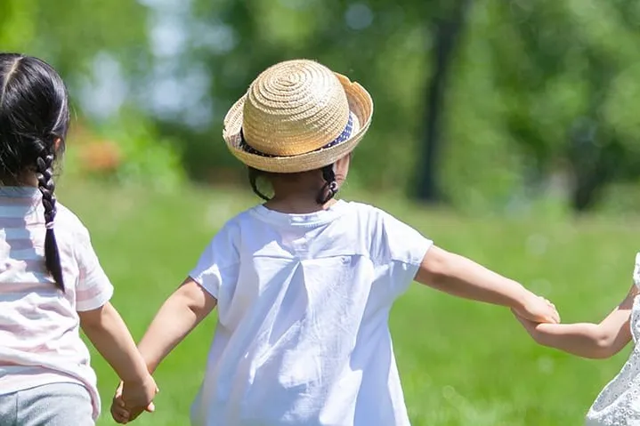 草原で手をつないで歩く3人の子どもの後ろ姿