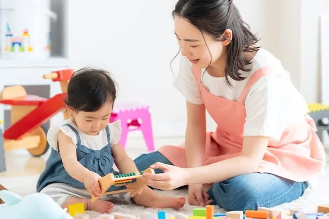 保育士と幼児が積み木のある部屋で遊ぶ様子