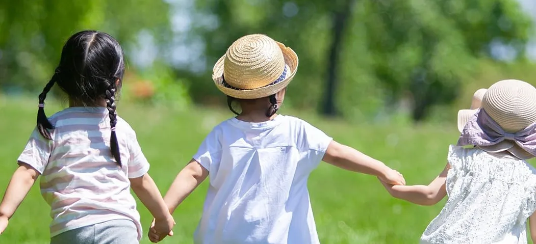 草原で手をつないで歩く3人の子どもの後ろ姿