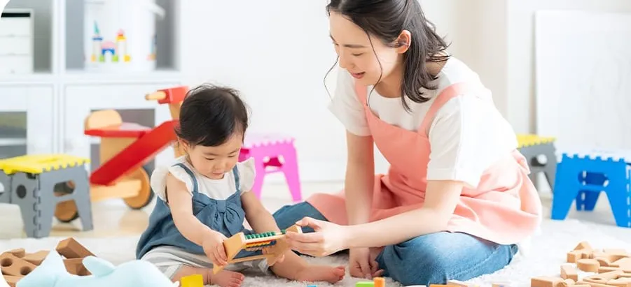 保育士と幼児が積み木のある部屋で遊ぶ様子